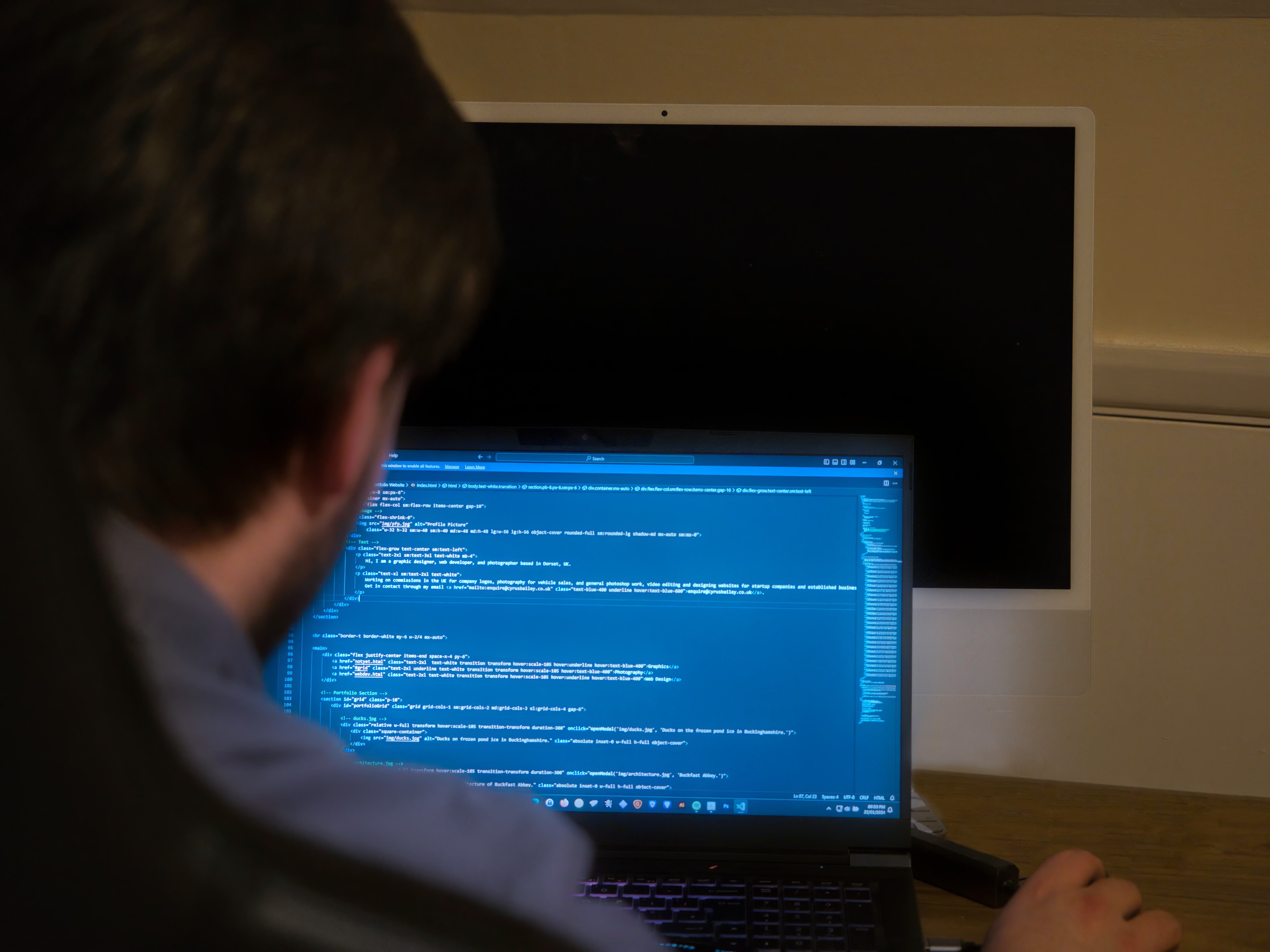 A photo of a man sitting in a chair, programming on a laptop.